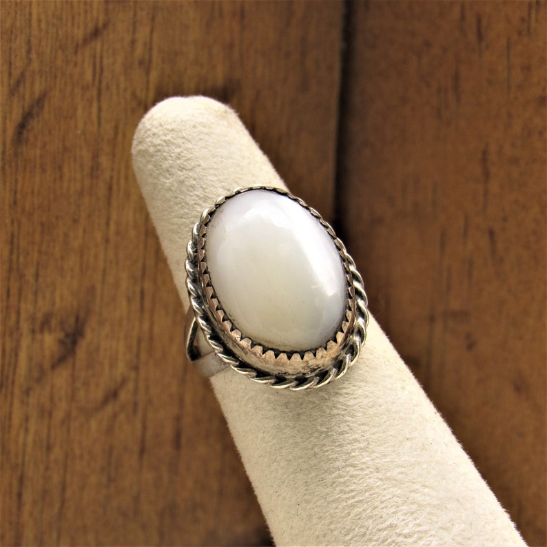 Puede incluir: Un anillo de plata con una piedra ovalada blanca engastada en un borde de cuerda.