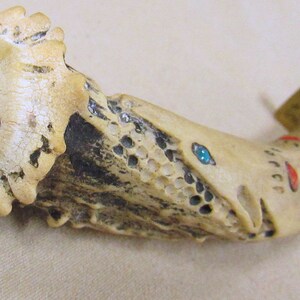 May include: A knife handle made of bone with turquoise and red accents. The handle is carved with a detailed design and has a brass cap.