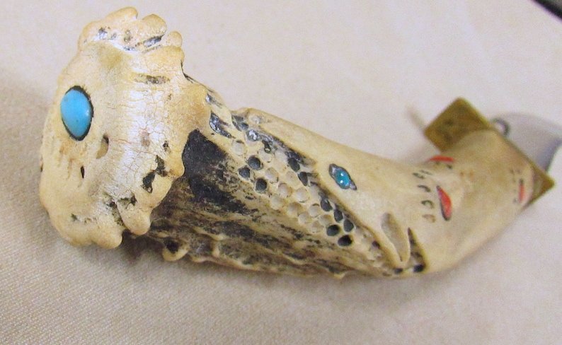May include: A knife handle made of bone with turquoise and red accents. The handle is carved with a detailed design and has a brass cap.