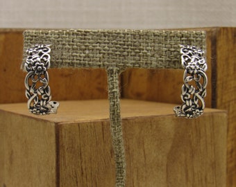 May include: A pair of silver hoop earrings with a floral design. The earrings are on a display stand.