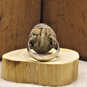 Puede incluir: Un anillo de plata con una gran piedra preciosa de forma ovalada. El anillo est&aacute; colocado sobre una superficie de madera.