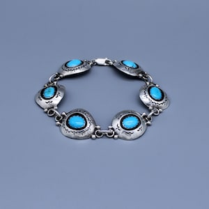 May include: A silver bracelet featuring seven oval turquoise stones set in decorative, scalloped settings. The bracelet is connected by small silver links and has a clasp closure. The turquoise stones are a vibrant blue color.