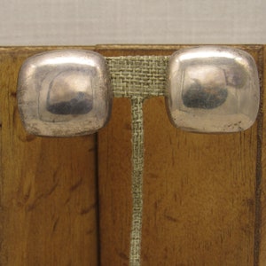 May include: A pair of silver square-shaped earrings. The earrings are smooth and have a slightly rounded shape.