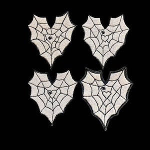 Peut inclure: Quatre patchs en forme de cœur blancs avec des toiles d'araignées noires et une araignée au centre de chaque toile.