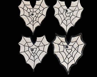 Op de afbeelding: Vier witte hartvormige patches met zwarte spinnenwebben en een spin in het midden van elk web.