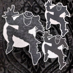 May include: Three black and white embroidered patches of a stylized figure in a dancing pose. The patches are on a black fabric background.
