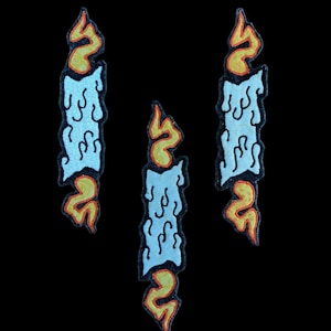 May include: Three embroidered patches depicting blue candles with orange and yellow flames. The candles are dripping wax and have a vintage cartoon style.
