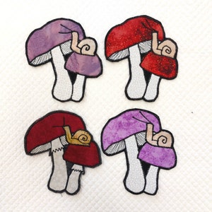 May include: Four felt mushroom appliques with snails on top. Two mushrooms are purple and two are red.