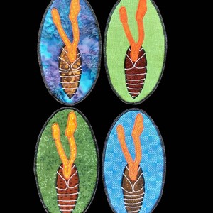 May include: Four fabric-covered oval-shaped ornaments with a brown, white, and orange design. The ornaments have a green, blue, and purple background.