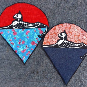 May include: Two felt patches with a skeleton cat design. The cat is lying down on a half-circle of red fabric with a floral pattern. The other half-circle is blue with a floral pattern.