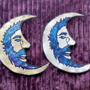 May include: Two crescent moon-shaped patches with a man's face on each. The faces are outlined in black and have a blue and white galaxy pattern. The moons are white with a yellow outline.