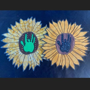 May include: Two yellow fabric sunflowers with handprints in the center. One handprint is green and the other is black and white.