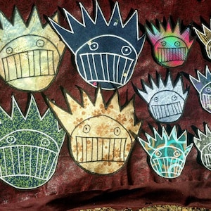 May include: Nine colorful fabric patches with a whimsical, cartoon-like design. Each patch features a smiling face with a large mouth and a crown of spikes. The patches are made of different fabrics and have a variety of colors and patterns.