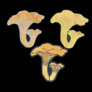 Puede incluir: Tres parches bordados para planchar con forma de seta de rebozuelo en diferentes colores: marrón claro, amarillo y marrón claro con contorno blanco.