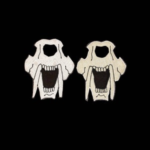 Może przedstawiać: Dwa haftowane naszywki przedstawiające czaszkę szablozębnego tygrysa, jedna biała, a druga beżowa.