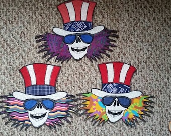 May include: Three embroidered patches featuring a skull wearing a top hat with red, white, and blue stripes and a bandana. Each patch has a different colored background with a psychedelic design.