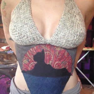 May include: A crocheted halter top with a paisley print and a denim triangle overlay. The top features a silhouette of a cat.