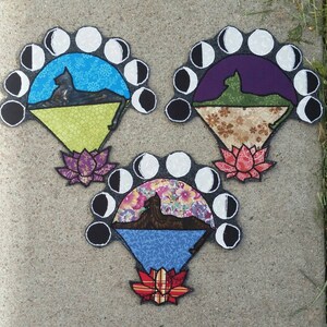 May include: Three embroidered patches featuring a cat silhouette against a crescent moon backdrop. Each patch has a different color scheme and floral design at the bottom. The patches are on a gray concrete surface.