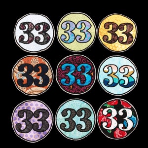 Puede incluir: Nueve parches redondos de tela con el número 33 en una variedad de colores y patrones. Los parches son todos del mismo tamaño y forma.