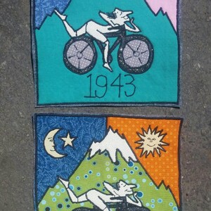 Pode incluir: Dois patches bordados com uma cena de montanha, uma pessoa de bicicleta e o ano de 1943. O patch superior tem um esquema de cores azul, rosa e verde. O patch inferior tem um esquema de cores azul, laranja, verde e branco.