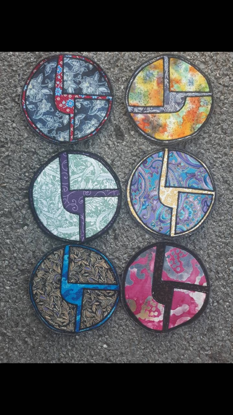 May include: Six round fabric patches featuring a geometric design in the shape of the letter L. The patches are made from different fabrics with a variety of patterns, including floral, paisley, and tie-dye.