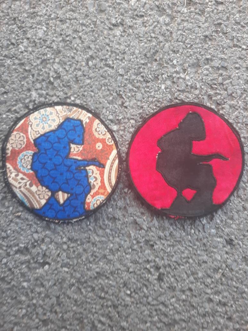 May include: Two round embroidered patches, one with a blue silhouette of a person on a paisley patterned background and the other with a black silhouette of a person on a red background.