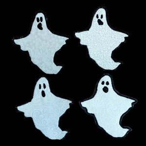 May include: Four light blue ghost-shaped appliqués with black outlines. Each ghost has a black open-mouthed expression. Two ghosts have a textured fabric, and two have a paisley pattern. The background is black.