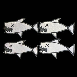 Könnte beinhalten: Vier weiße, gestickte Bügelbilder von Haien mit schwarzen Umrissen und einem X für die Augen. Die Haie haben einen offenen Mund mit Zähnen.
