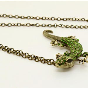 May include: A gold chain necklace with a green jeweled lizard pendant.