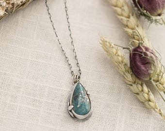May include: A silver chain necklace with a teardrop-shaped pendant featuring a blue-green gemstone set in silver.