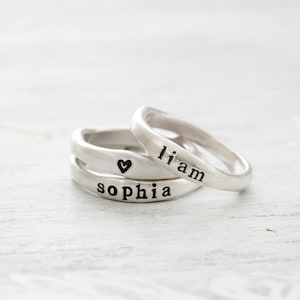 May include: Two silver rings with the names "Liam" and "Sophia" engraved on them. A small heart symbol is engraved on the ring with the name "Sophia".