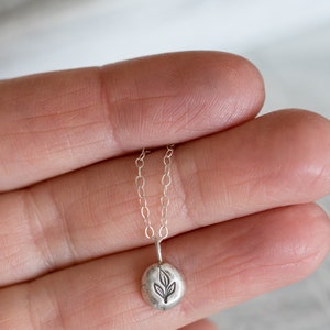 Puede incluir: Un collar de plata con un peque&ntilde;o colgante redondo con un dise&ntilde;o de hoja.