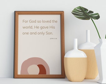 Puede incluir: Una impresión enmarcada con un fondo beige y un diseño abstracto marrón, rosa y blanco. La impresión presenta el texto "For God so loved the world, He gave His one and only Son." con la referencia bíblica "John 3:16". La impresión está sobre una superficie blanca con dos jarrones y una planta verde con hojas.
