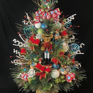 May include: A miniature Christmas tree decorated with red and white bows, blue and green ornaments, white snowflakes, and a nutcracker figurine.