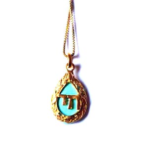 Peut inclure: Un collier doré avec un pendentif en forme de goutte doté d'une bordure texturée. Le centre du pendentif présente une incrustation turquoise vive avec un caractère hébreu doré au milieu du champ bleu, le tout suspendu à une chaîne.