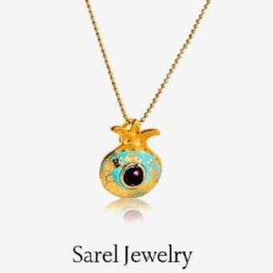 Peut inclure: Un collier dor&eacute; avec un pendentif en forme de grenade. Le pendentif est orn&eacute; d'&eacute;mail turquoise et d'une pierre rouge fonc&eacute; au centre. Le texte "Sarel Jewelry" est visible en dessous.