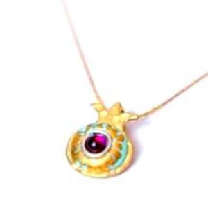 Peut inclure: Un collier pendentif dor&eacute; repr&eacute;sentant une grenade. Le pendentif est orn&eacute; d'une pierre pr&eacute;cieuse rouge ronde au centre et de d&eacute;tails turquoise. La cha&icirc;ne du collier est fine et dor&eacute;e.