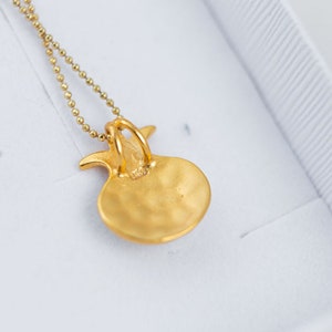 Peut inclure: Un collier pendentif dor&eacute; avec un design de grenade. Le pendentif a une surface textur&eacute;e et est suspendu &agrave; une fine cha&icirc;ne &agrave; billes. Le collier est pr&eacute;sent&eacute; dans une bo&icirc;te blanche avec un int&eacute;rieur textur&eacute;.
