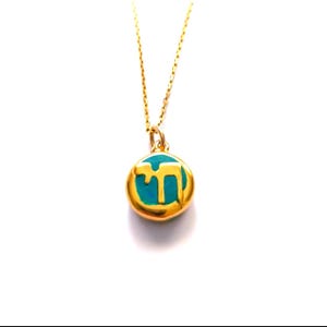 Peut inclure: Un collier à chaîne dorée avec un pendentif circulaire doté d'un bord doré poli et d'un centre bleu turquoise vif. Le pendentif présente une lettre hébraïque Chai dorée en relief au milieu, suspendu à une fine chaîne à maillons dorés.