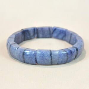 May include: A blue gemstone bracelet. The bracelet is made of rectangular, polished blue stones. The stones have a marbled appearance with darker blue veins. The bracelet is a continuous loop, designed to be worn around the wrist.