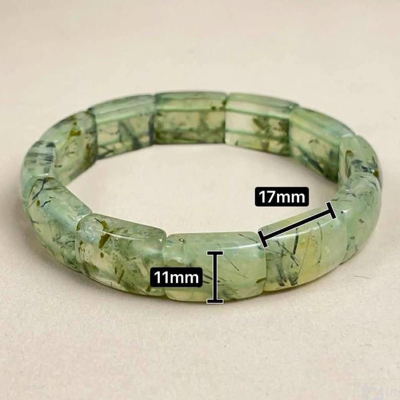 May include: A light green prehnite bracelet. The bracelet is made of rectangular beads, each measuring 11mm x 17mm. The beads have a translucent quality with darker green inclusions. The bracelet is displayed on a neutral background.