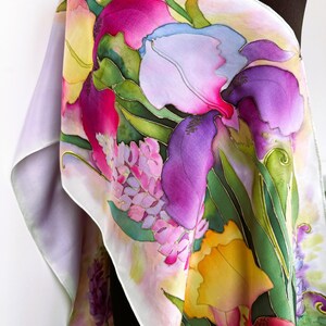 K&ouml;nnte beinhalten: Ein rechteckiger Seidenschal mit einem handgemalten Blumenmuster in leuchtenden Magenta-, Violett-, Gelb- und Gr&uuml;nt&ouml;nen. Das Design zeigt gro&szlig;e, irisartige Bl&uuml;ten und l&auml;ngliche Bl&auml;tter mit klar definierten Umrissen auf einem hellen Hintergrund.