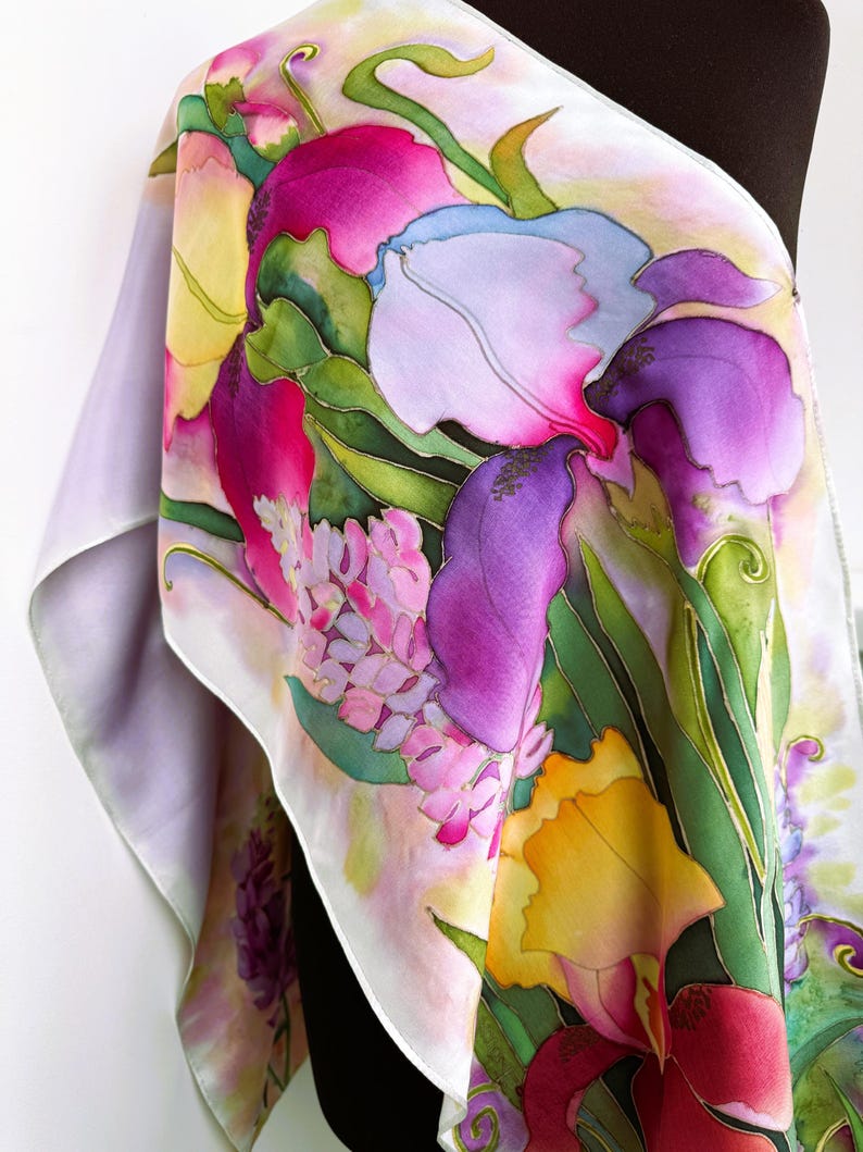 K&ouml;nnte beinhalten: Ein rechteckiger Seidenschal mit einem handgemalten Blumenmuster in leuchtenden Magenta-, Violett-, Gelb- und Gr&uuml;nt&ouml;nen. Das Design zeigt gro&szlig;e, irisartige Bl&uuml;ten und l&auml;ngliche Bl&auml;tter mit klar definierten Umrissen auf einem hellen Hintergrund.