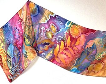 Puede incluir: Una bufanda de seda colorida con un diseño floral. La bufanda presenta una variedad de colores, incluyendo naranja, amarillo, rosa, morado y azul. El diseño incluye hojas, flores y otros elementos botánicos.