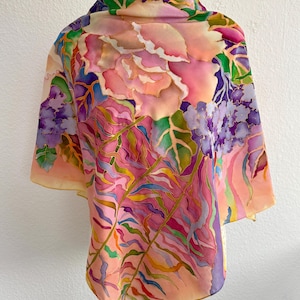 May include: A lightweight scarf featuring a hand-painted floral design with large pink roses, purple hydrangea clusters, and long green fern fronds. The fabric displays a vibrant color palette of pink, purple, green, and orange hues with defined outlines.