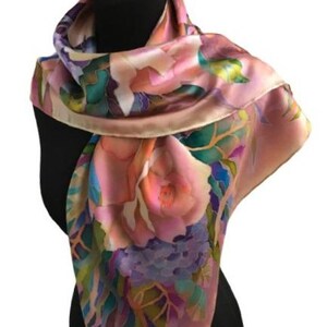 May include: A square silk scarf featuring a hand-painted floral pattern in shades of soft pink, deep teal, lavender, and muted green. The design displays large, blooming flowers and leafy foliage with blended color transitions and a smooth finish.