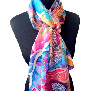 May include: A colorful silk scarf with a floral and abstract design in shades of pink, blue, yellow, and orange. The scarf is tied around a black mannequin's neck.