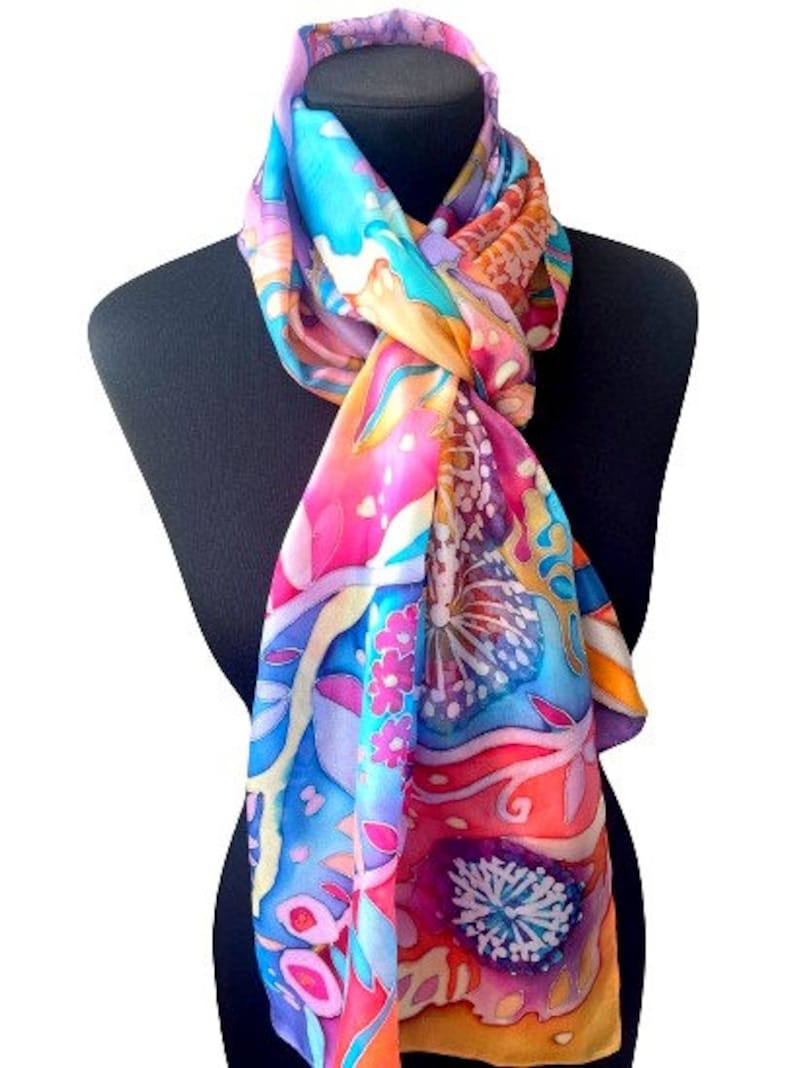 May include: A colorful silk scarf with a floral and abstract design in shades of pink, blue, yellow, and orange. The scarf is tied around a black mannequin's neck.