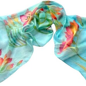 Pode incluir: Um len&ccedil;o leve e semitransparente em azul turquesa brilhante. O tecido apresenta um padr&atilde;o floral pintado &agrave; m&atilde;o com flores vibrantes em tons de rosa, laranja e amarelo, juntamente com caules e folhas verdes por toda a superf&iacute;cie.