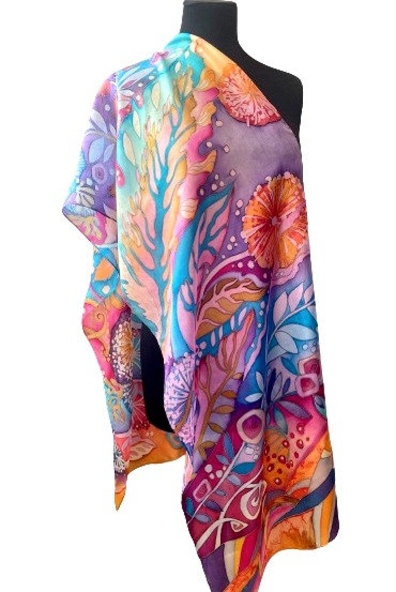 May include: A colorful silk scarf with a floral pattern in shades of pink, blue, yellow, and orange. The scarf is draped over a mannequin's shoulders.
